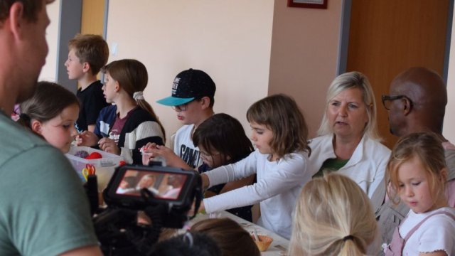Das Foto zeigt: Ortsbürgermeisterin Beate Sommerfeld und Yared Dibaba im Gespräch. Sie sitzen an einem Tisch, um sie herum basteln Kinder.