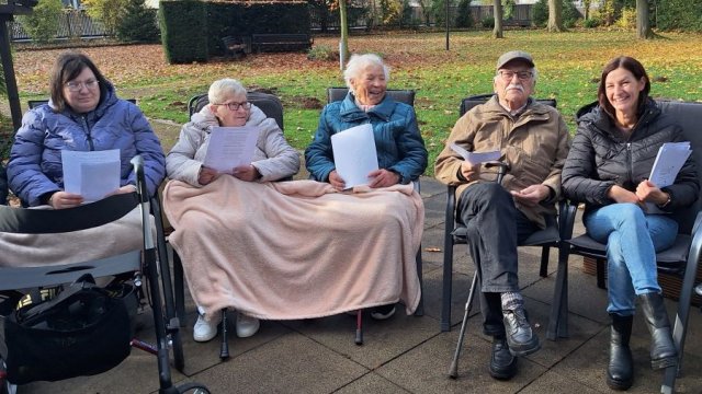 Das Foto zeigt Menschen, die in einer Reihe im Garten sitzen, teilweise gegen die Kälte geschützt mit einer Decke über den Beinen.